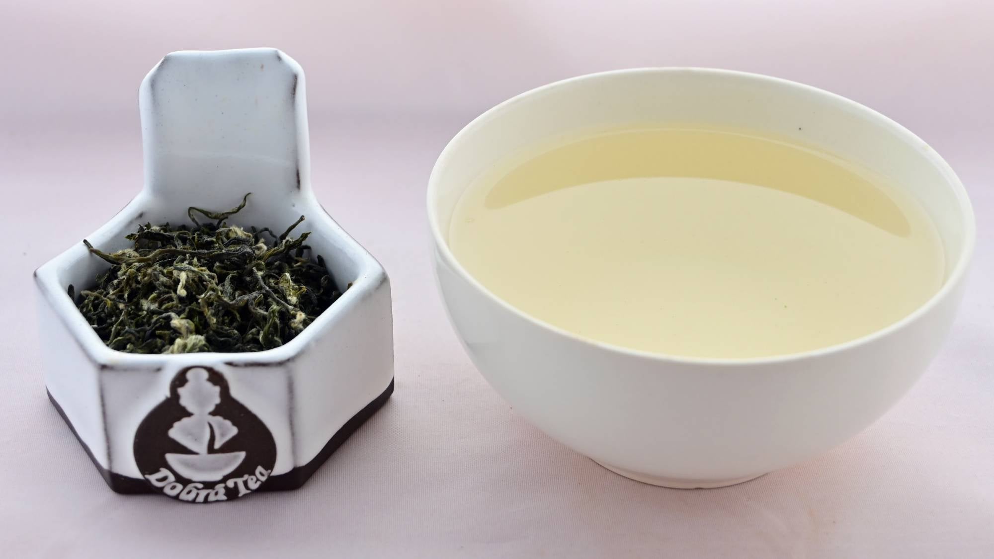 A side-by-side comparison of Bi Lou Chun leaves and steeped tea. On the left, the leaves range from bright green to dark green. They are twisted and curling, and appear slightly fuzzy. On the right, the steeped tea is a pale yellow color.