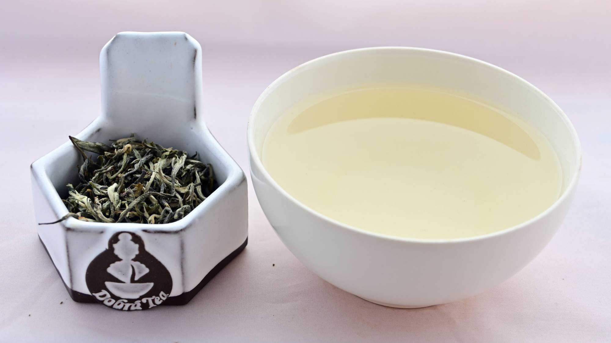 A side by side comparison of Dian Lu Wenshan leaves and steeped tea. On the left, the tea leaves are predominantly pale green and twisted into zig-zaging rolls. On the right, the steeped tea is a pale yellow.