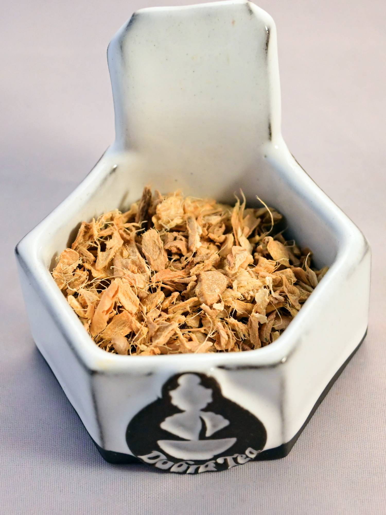 A close-up of dried ginger root. The herb is a pale orange color and has many fibrous strings.