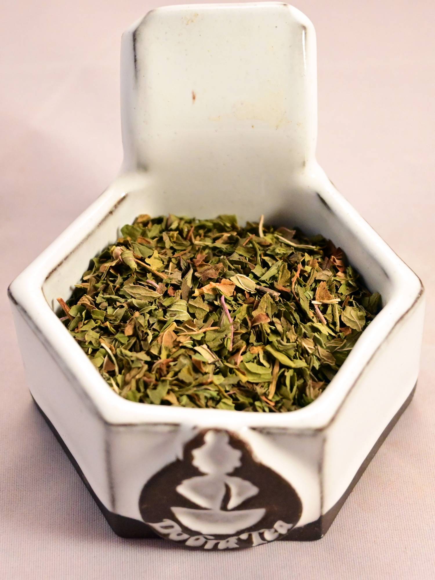 A close-up of dried peppermint. There are a collection of tiny leaves ranging in color from dark green to light green, with a few orange leaves in the mixture.