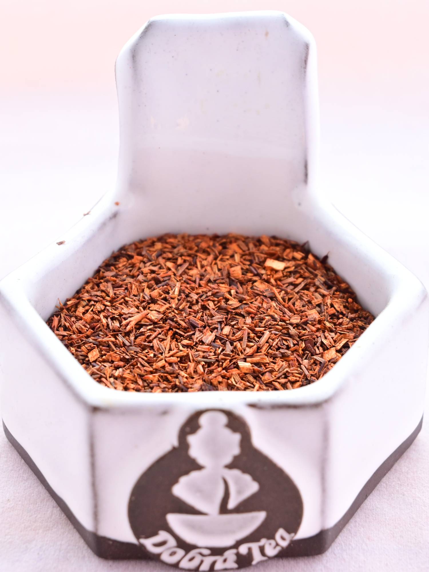 A close-up of the dried Red Rooibos herb. It is a red-orange color, and maid of small, stem-looking slices as long as they are wide.