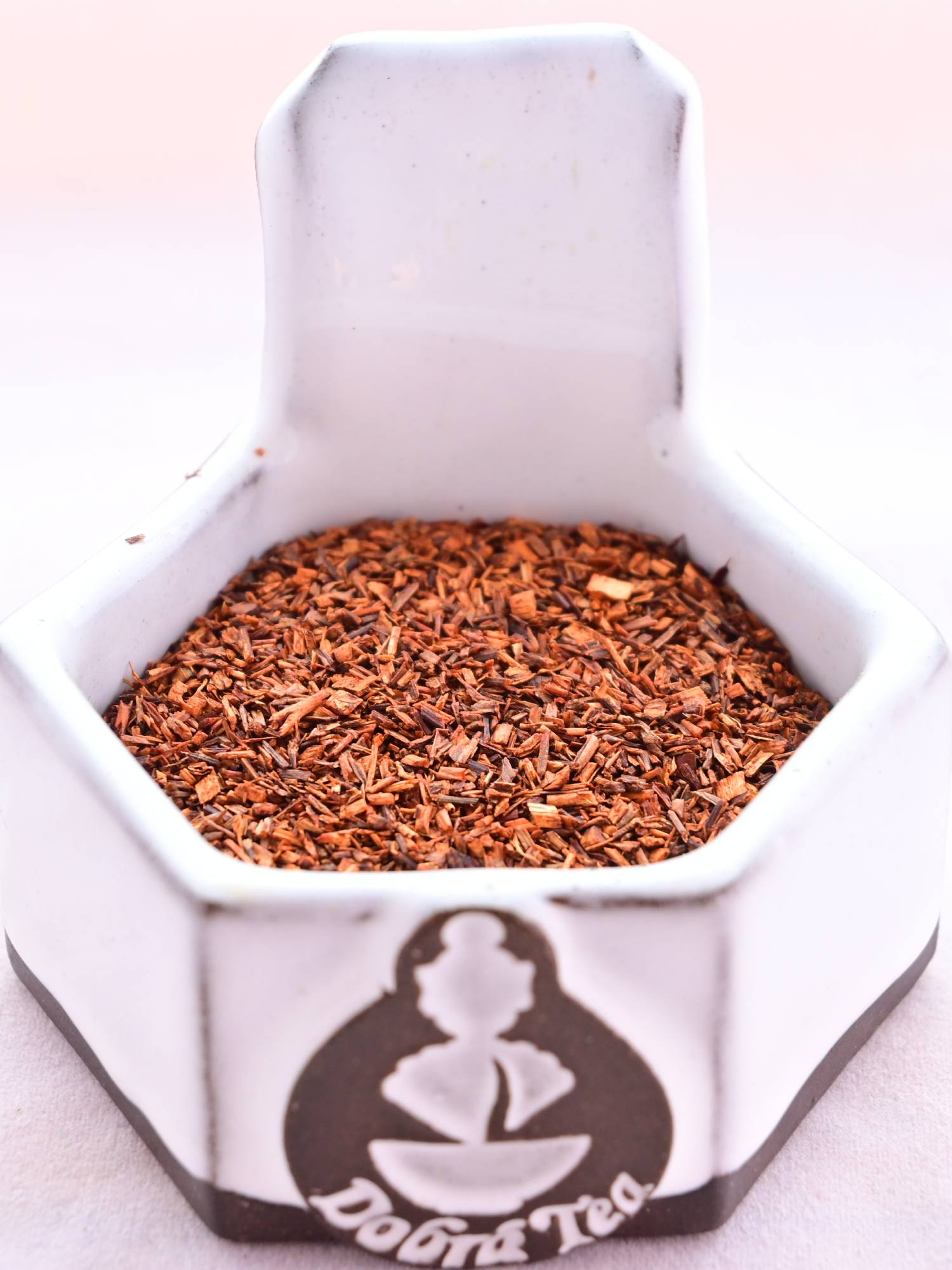 A close-up of the dried Red Rooibos herb. It is a red-orange color, and maid of small, stem-looking slices as long as they are wide. 