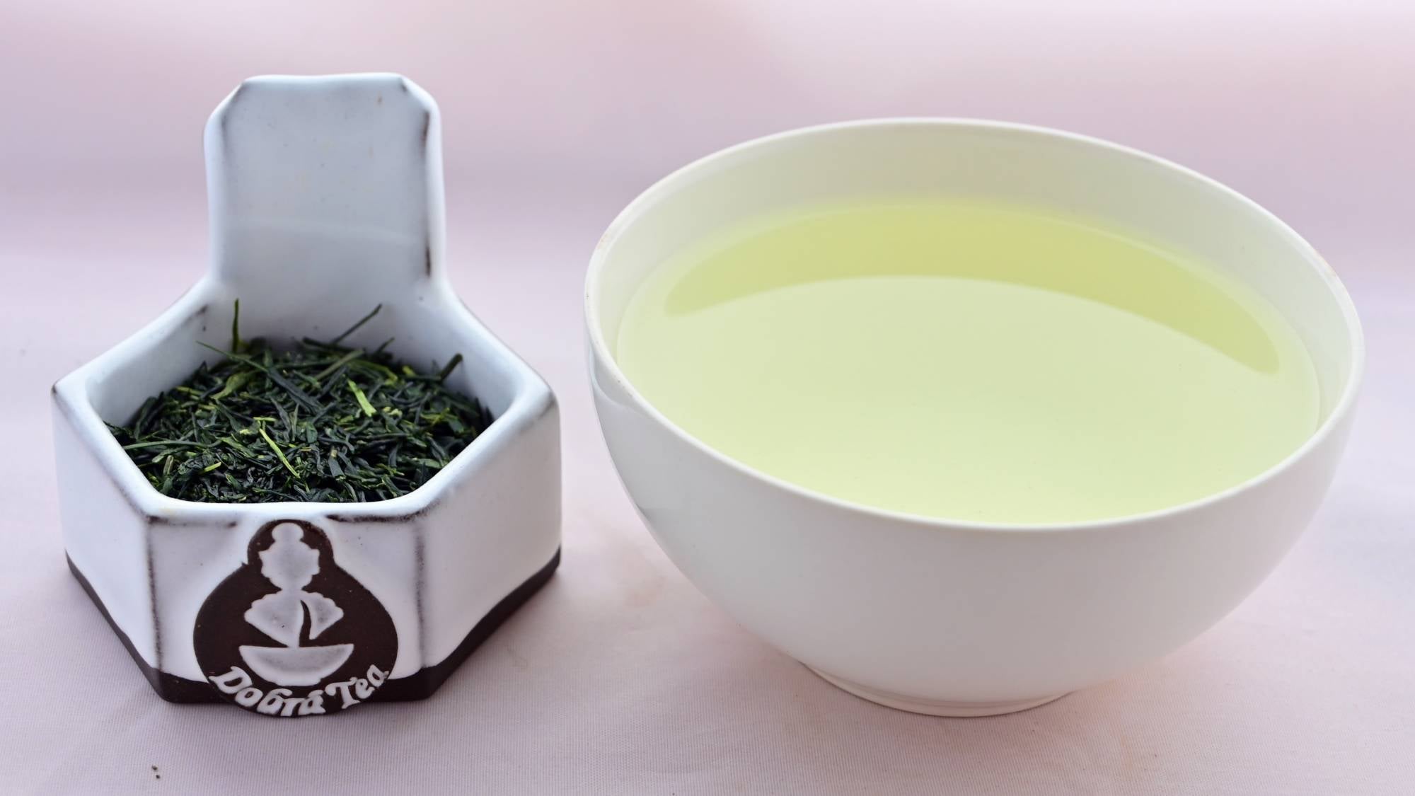 A side-by-side comparison of Shincha leaves and steeped tea. On the left, the leaves are predominantly dark green, long, flat, and narrow. On the right, the steeped liquid is a pale green.