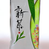 The Shincha package is mainly white, with green patterning on the right side. Inside one of the green semi-circles is a group of red and yellow flowers. On the left size of the plastic package are Japanese letters followed by a tea leaf.