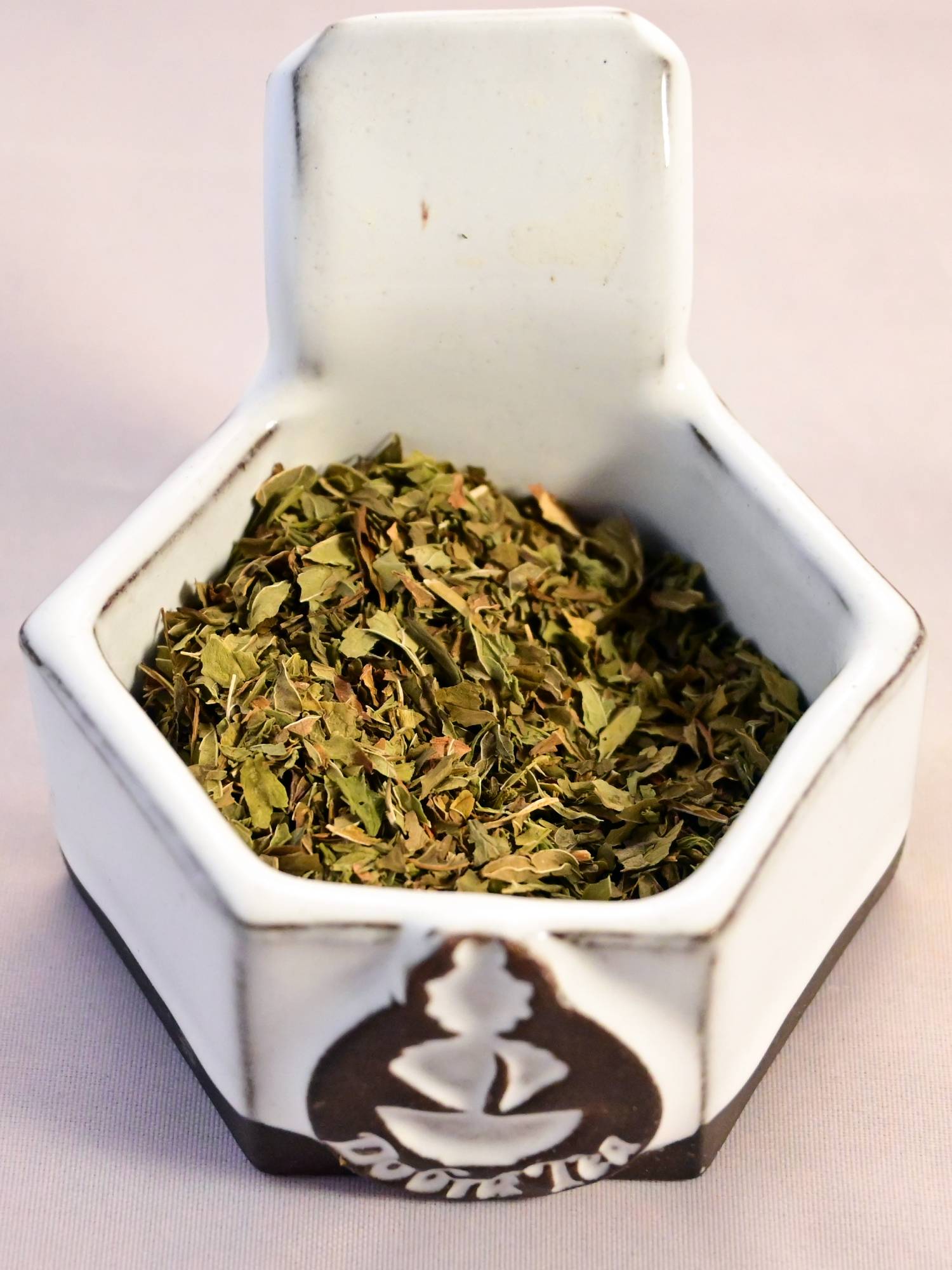 A close-up of dried spearmint leaf. The leaves are small and individually dried, and range in color from light green to dark green.