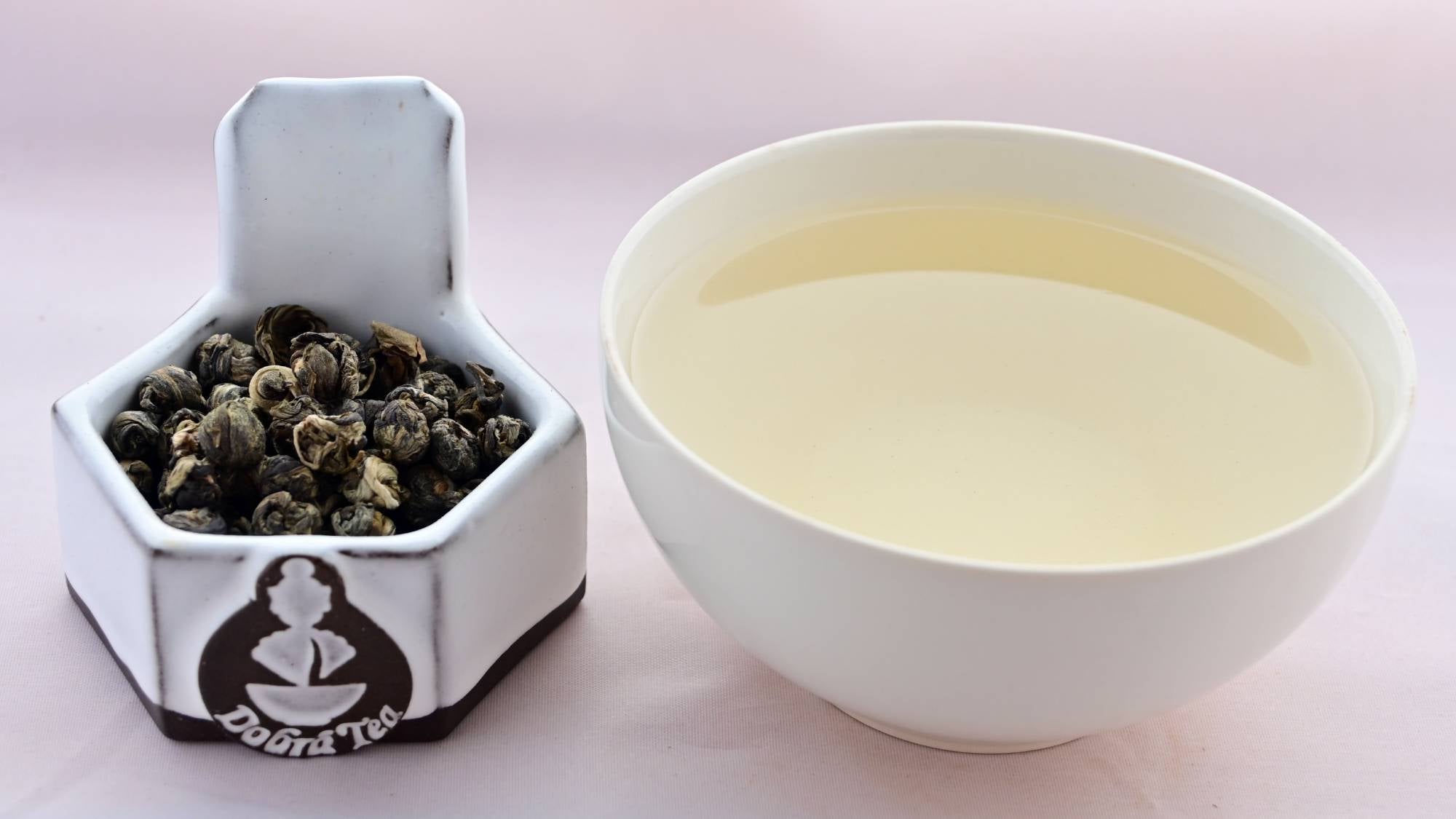 A side-by-side comparison of Taimu Long Zhu leaves and steeped tea. On the left, the leaves are curled into tight balls the size of finger-nails. They range in color from dark green to pale green. On the right, the steeped liquid is pale yellow.