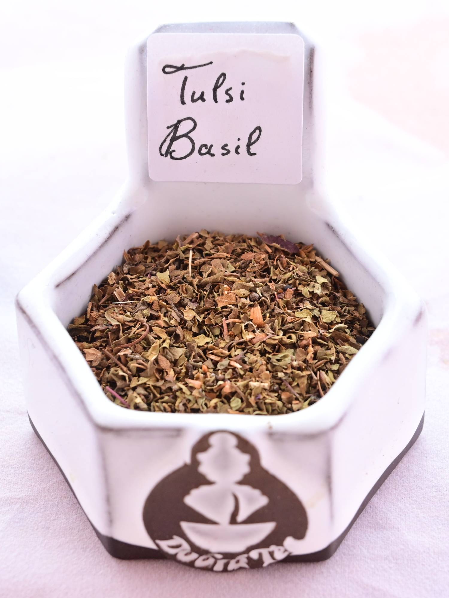 A close-up of Tulsi Holy Basil leaves. They are small, dust-like and range in color from green to brown, with splashes of orange.