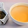 A side-by-side comparison of the tulsi herb and steeped tisane. On the left, the tulsi leaves are small, dust-like and range in color from green to brown. On the right, the steeped tisane is a soft orange color.