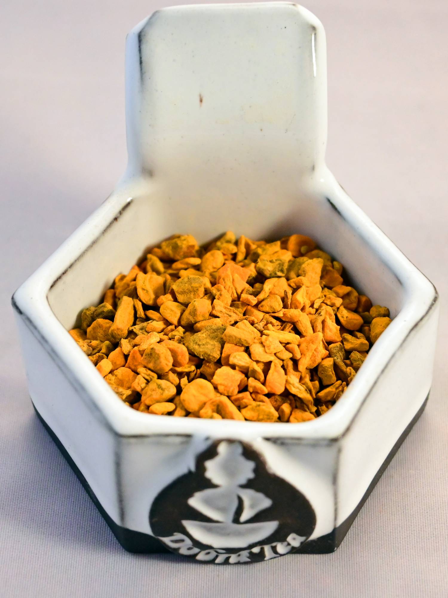 A close-up of dried turmeric root. The small pellets are a bright orange color.