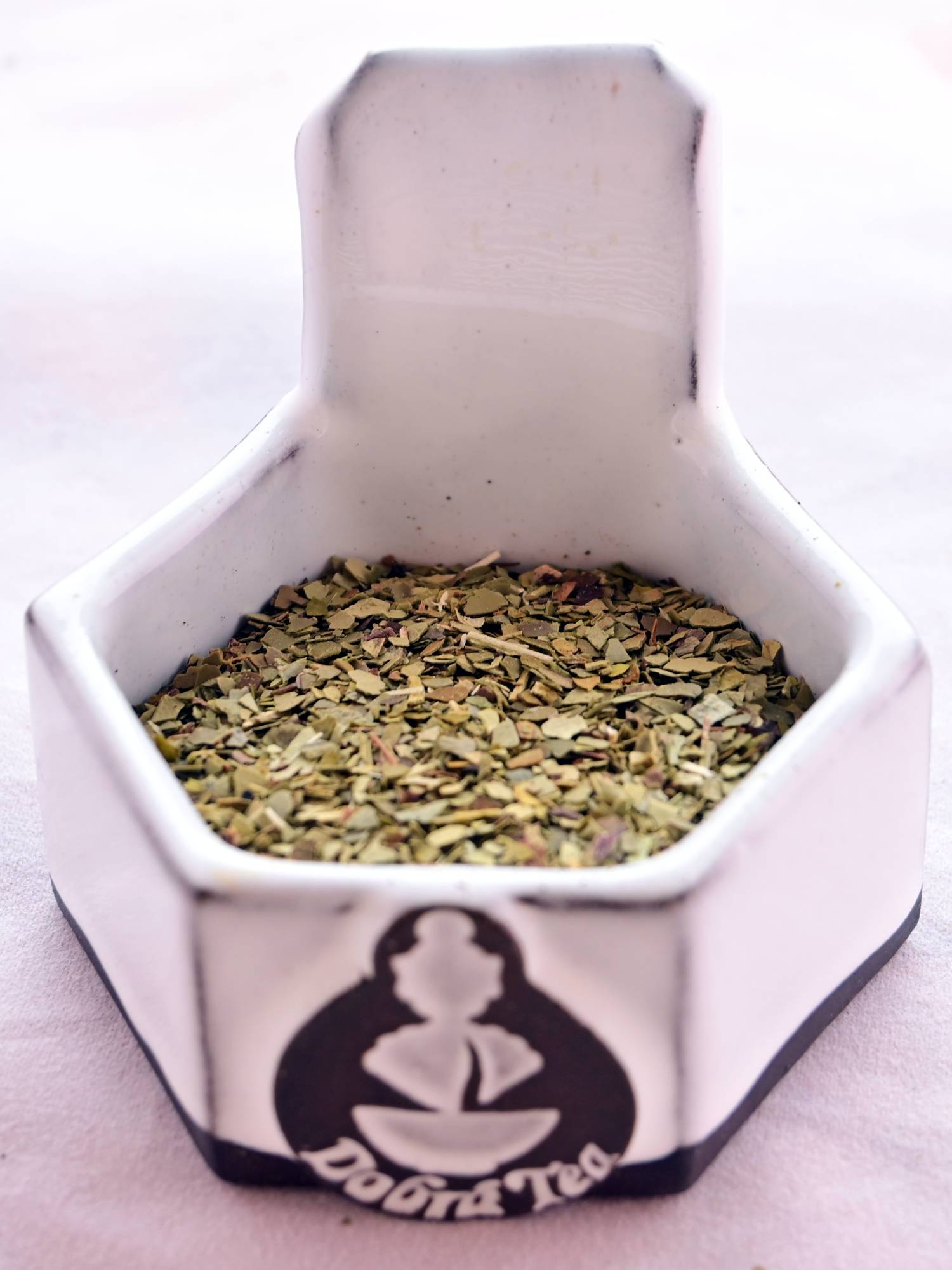 A close-up of Yerba Mate dried leaves. The flakes are small, flat, and relatively circular. They range in color from pale brown to green-brown.