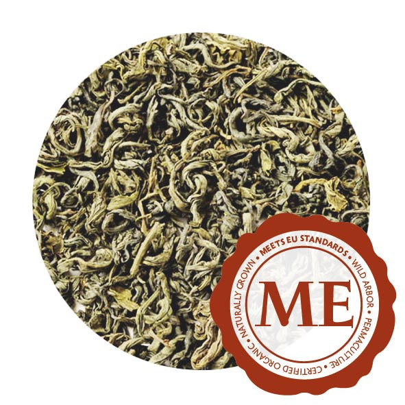 A close-up of Che Xanh leaves. They are a pale green color. They are tightly curled into spirals and coils. They have a Meets EU Standards certification.