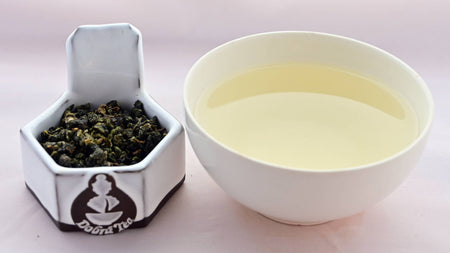 Ali Shan tea leaves on the left, tightly rolled into finger nail sized balls. On the right is cup with pale yellow tea from steeping the leaves.