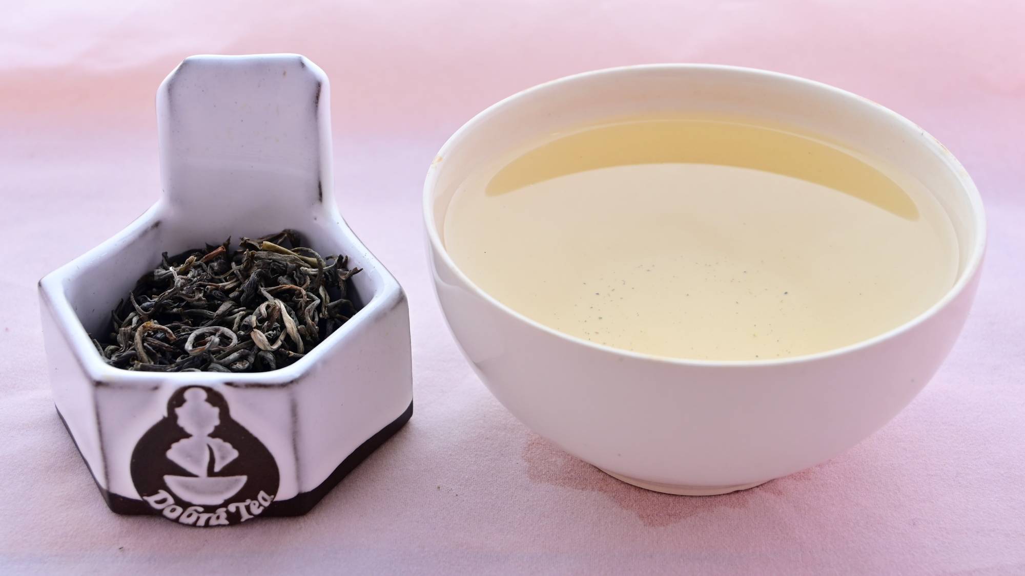 A side-by-side comparison of Ancient Arbor (Ha Giang Che Xanh) leaves and steeped tea. On the left, the leaves are curled around nearly into circles. They are dark green with the occasional light green tossed in. On the right, the steeped tea is a pale yellow.