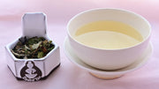 A side-by-side comparison of Bai Mu Dan leaves and steeped tea. On the left, the leaves are flat and large, and have a green tint. On the right, the steeped tea is a pale yellow.