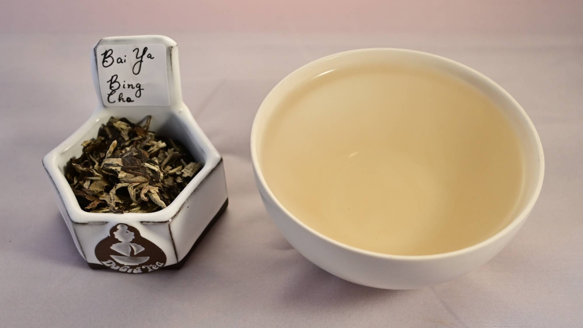 Bai Ya Bing Cha tea leaves on the left, steeped tea on the right. The steeped tea has a pale peach color.
