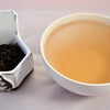 A side-by-side comparison of Bamboo Pu'er leaves and tea. The leaves on the left are dark grown and shadowy. The tea on the right is a warm red-brown.