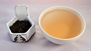 A side-by-side comparison of Bamboo Pu'er leaves and tea. The leaves on the left are dark grown and shadowy. The tea on the right is a warm red-brown.