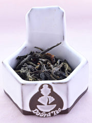 A close-up of Burmese Wild Green tea leaves, showing loosely twisted and flowing leaves that range from dark brown to black.