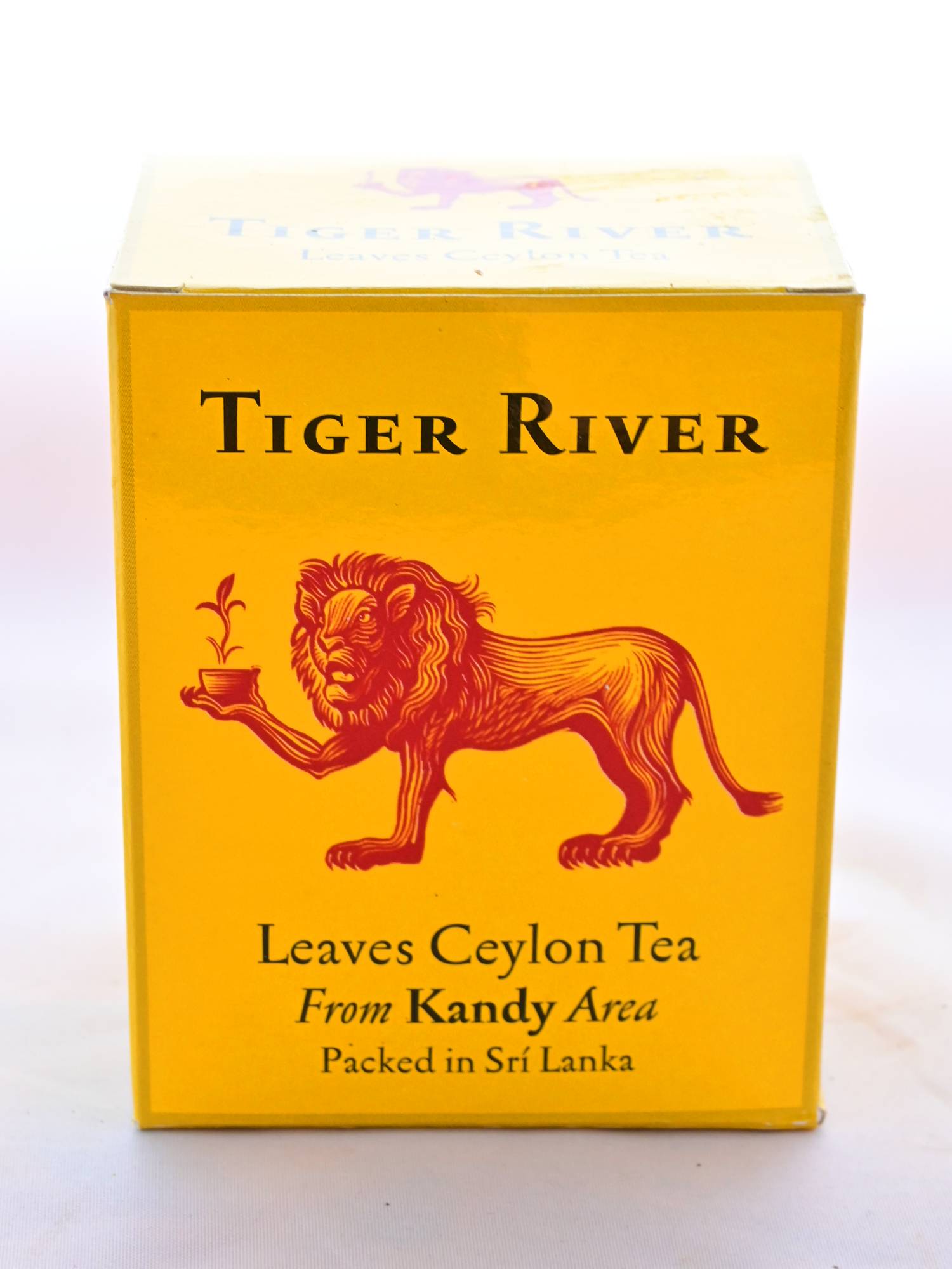 The Ceylon Tiger River box is orange with a red lion holding a flowering tea cup drawn in the center. English lettering reads: "Tiger River. Leaves Ceylon Tea. From Kandy Area. Packed in Sri Lanka."