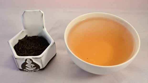 A side-by-side comparison of Ceylon Adam's Peak leaves and steeped tea. On the left, the leaves are all small, uniform, and brown like 80% cocoa. On the right, the steeped tea is a rich orange color.
