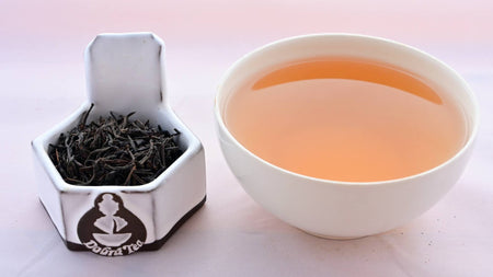 A side-by-side comparison of Ceylon Tiger River leaves and steeped tea. On the left, the leaves are a black color, and resemble small twigs. On the right, the steeped tea has a brown-red color.