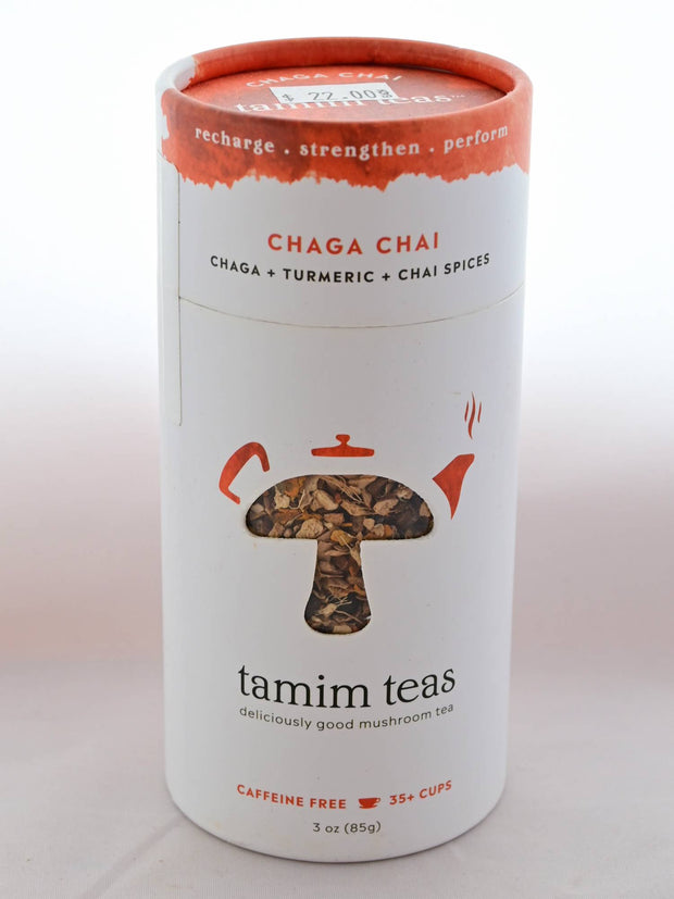 The Chaga Chai tin is cylindrical and mostly white with a splash of orange on top. In the middle, a clear cutout in the shape of a mushroom shows part of the blend, with orange tea pot decorations around the mushroom's crown. Text reads: "Recharge. Strengthen. Perform. Chaga Chai. Chaga and tumeric and chai spices. tamim teas. deliciously good mushroom tea. Caffeine free. 35+ cups. 3 oz (85 grams)."