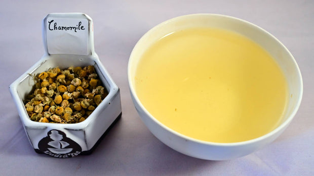 A side-by-side comparison of dried chamomile buds and steeped tea. On the left, the dried buds are about the size of your smallest finger nail and are pale yellow in color. On the right, the steeped liquid is the exact color of the chamomile buds.
