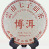 A Chi Tse Bing Cha disk is shown on a black book stand. The disk is wrapped in a white tissue paper decorated in red. Chinese letters circle the outside, with English translations underneath: "Black Pu Erh Beengcha. Spring 2014. 357 grams."