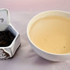 A side-by-side comparison of Da Hong Pao leaves and steeped tea. On the left, the leaves are dark brown and loosely curled. On the right, the steeped tea is a soft peach.