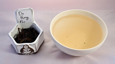 A side-by-side comparison of Da Hong Pao leaves and steeped tea. On the left, the leaves are dark brown and loosely curled. On the right, the steeped tea is a soft peach.