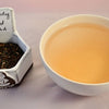 A side-by-side comparison of Darjeeling Second Flush leaves and steeped tea. On the left, the leaves are dark brown with spots of pale green. On the right, the steeped tea is a pale orange color.