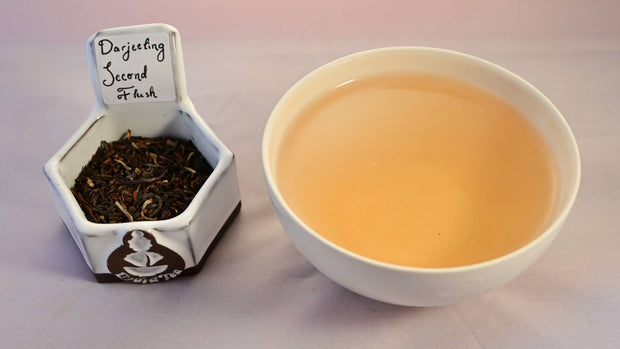 A side-by-side comparison of Darjeeling Second Flush leaves and steeped tea. On the left, the leaves are dark brown with spots of pale green. On the right, the steeped tea is a pale orange color.