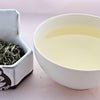 A side by side comparison of Dian Lu Wenshan leaves and steeped tea. On the left, the tea leaves are predominantly pale green and twisted into zig-zaging rolls. On the right, the steeped tea is a pale yellow.