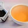 A side-by-side comparison of Earl Grey leaves and steeped tea. On the left, the leaves are black and spiraled loosely. On the right, the steeped tea is a ruddy orange.