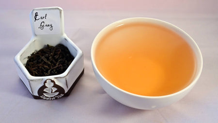 A side-by-side comparison of Earl Grey leaves and steeped tea. On the left, the leaves are black and spiraled loosely. On the right, the steeped tea is a ruddy orange.