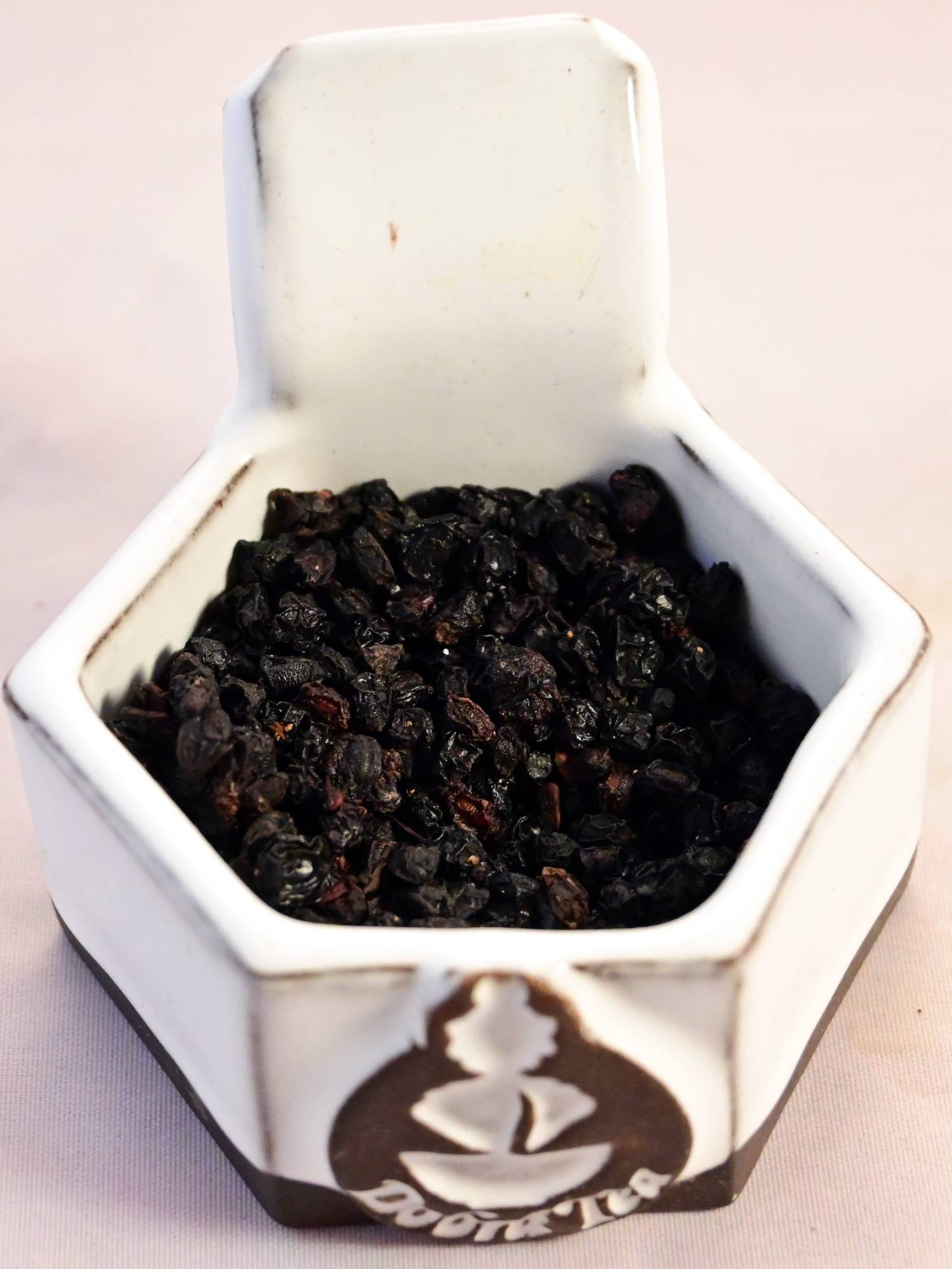 A close-up of dried elder berries. They are black with red undertones, and resemble raisins.