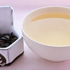 A side-by-side comparison of Feng Huang Dan Cong leaves and steeped tea. On the left, the leaves are dark brown and withered, drooping like dog's ears. On the right, the steeped tea is a dull yellow.
