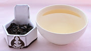 A side-by-side comparison of Feng Huang Dan Cong leaves and steeped tea. On the left, the leaves are dark brown and withered, drooping like dog's ears. On the right, the steeped tea is a dull yellow.