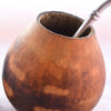 The traditional drinking set up for Guayusa, featuring a brown gourd with a circle cut out at the top. A metal straw comes from inside the gourd and hangs to the right.