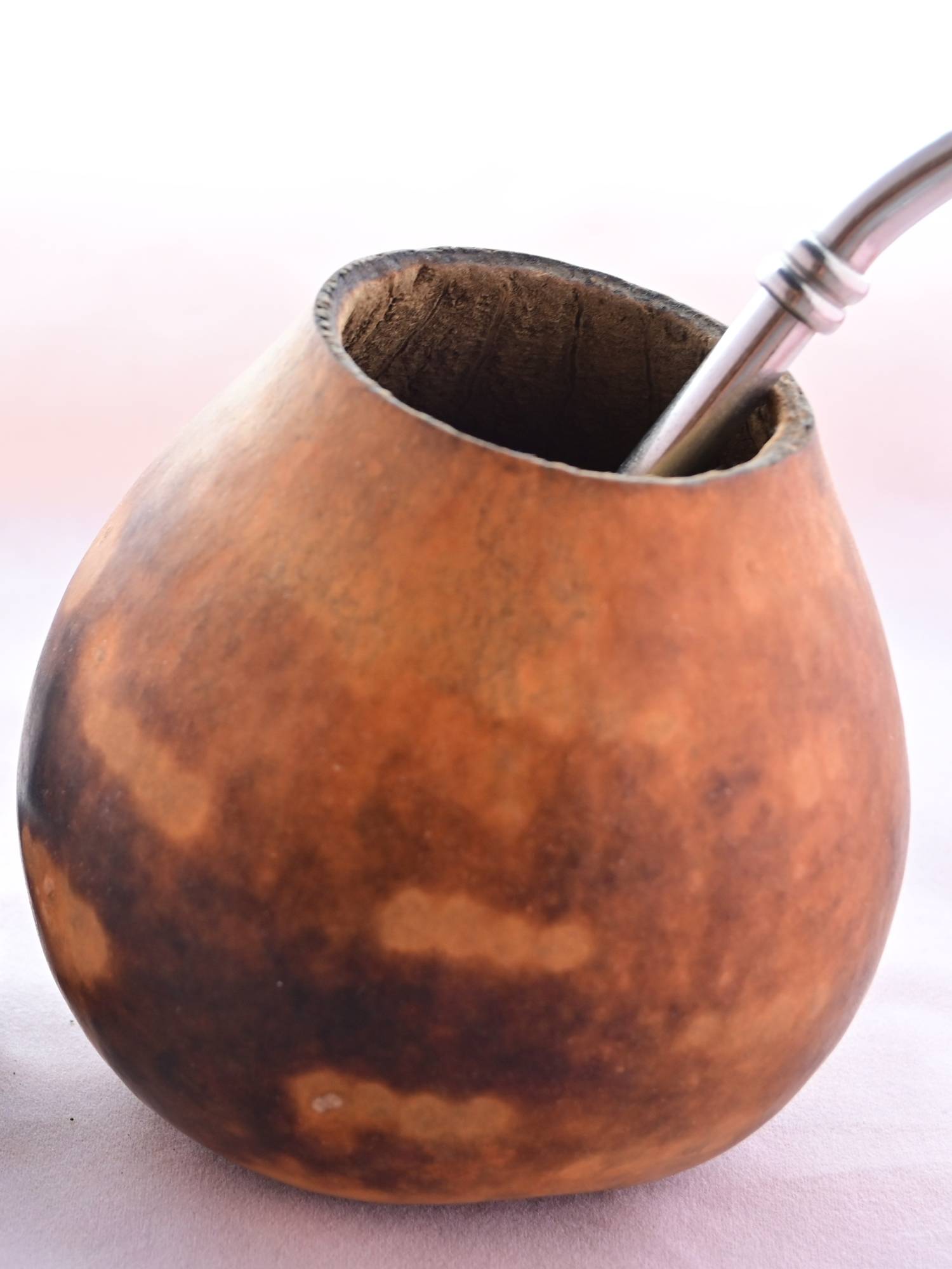 The traditional drinking set up for Guayusa, featuring a brown gourd with a circle cut out at the top. A metal straw comes from inside the gourd and hangs to the right.