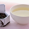 A side-by-side comparison of Gui Fei leaves and steeped tea. On the left, the leaves are small and have been rolled into crumpled, dark pellets. On the right, the steeped tea is a pale yellow.