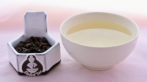 A side-by-side comparison of Gui Fei leaves and steeped tea. On the left, the leaves are small and have been rolled into crumpled, dark pellets. On the right, the steeped tea is a pale yellow.