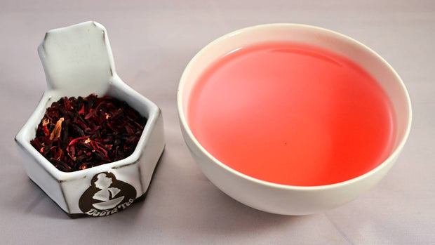 A side-by-side comparison of dried hibiscus petals and steeped tea. On the left, the dried herb ranges in color from rose to dark red. On the right, the steeped liquid is a bright blood orange color.