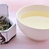 A side-by-side comparison of Huang Ya leaves and steeped tea. On the left, the leaves are long and thick, resembling dried yellow buds more than traditional leaves. On the right, the steeped tea is a pale yellow.