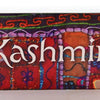 The paper Taste of Kashmir box features intricate designs and decorations, as though someone hand-embriodered a red and brown blanket with orange, green, purple, blue and other threads. White text reads: "Kashmir."