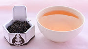 A side-by-side comparison of Kenyan FOP leaves and steeped tea. On the left, the leaves are small, black, and tightly curled. On the right, the steeped tea is a rich orange color.