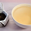 A side-by-side comparison of Lao Shu Bing Cha leaves and steeped tea. On the left, the leaves are dark brown to black, and flaky. On the right, the liquid is a pale peach color.