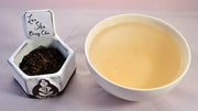 A side-by-side comparison of Lao Shu Bing Cha leaves and steeped tea. On the left, the leaves are dark brown to black, and flaky. On the right, the liquid is a pale peach color.