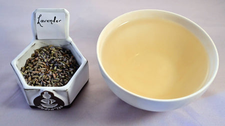 A side-by-side comparison of dried lavender buds and steeped tea. On the left, the dried lavender buds are a faint periwinkle. On the right, the steeped liquid is pale yellow.
