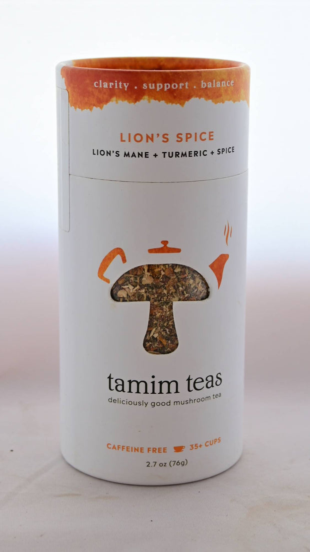 The Lion's Spice tin is cylindrical and mostly white with a splash of orange on top. In the middle, a clear cutout in the shape of a mushroom shows part of the blend, with orange tea pot decorations around the mushroom's crown. Text reads: "Clarify. Support. Balance. Lion's Spice. Lion's Mane and turmeric and spice. tamim teas. Deliciously good mushroom tea. Caffeine free. 35+ cups. 2.7 oz (76 grams)."
